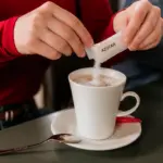 Persona echando monodosis azúcar café leche